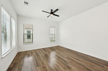 A room with a ceiling fan and two windows.
